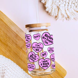 Puede incluir: Un vaso de vidrio transparente con tapa de bamb&uacute; y pajita transparente. El vaso est&aacute; decorado con pegatinas rosas en forma de coraz&oacute;n con varias frases en texto negro, incluyendo "Bitches Are People Too" y "I wish a bitch would".
