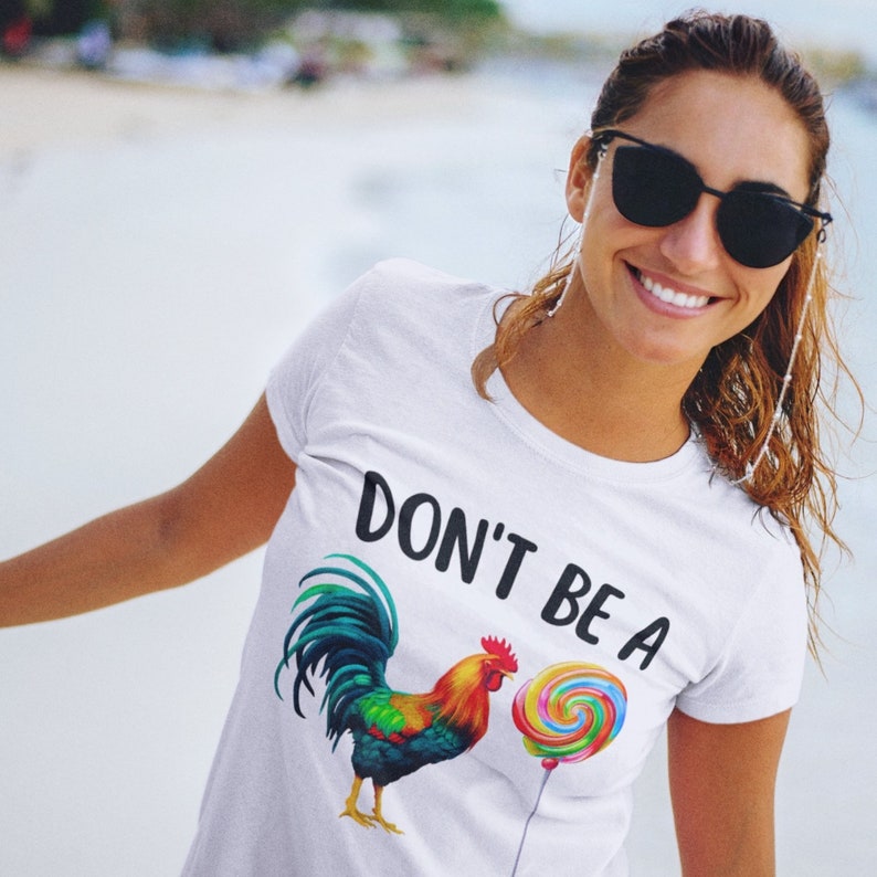 May include: White t-shirt with the text "Don't be a" and a colorful rooster illustration holding a rainbow lollipop.