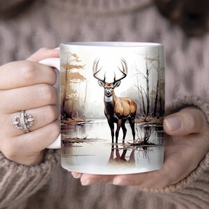 May include: White ceramic mug with a brown and white illustration of a deer standing in a lake with trees in the background.