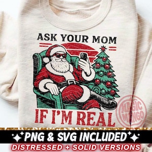 Puede incluir: Sudadera color crema con un gráfico de Papá Noel con gafas de sol, sosteniendo un teléfono y sentado en una silla. El texto dice "ASK YOUR MOM IF I'M REAL". Un árbol de Navidad está a la derecha.