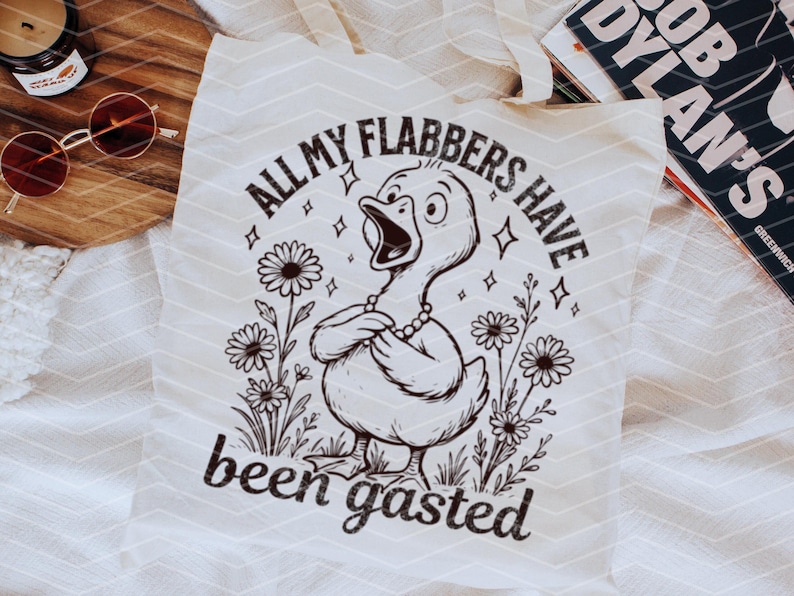 以下が含まれることがあります： 白いトートバッグに、白黒の鴨のイラストと「All my flabbers have been gasted」というテキストが描かれています。