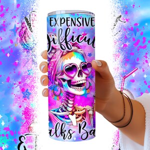 May include: A pink and purple stainless steel tumbler with a colorful skull design and the text "Expensive Tastes Difficult Walks Backwards".