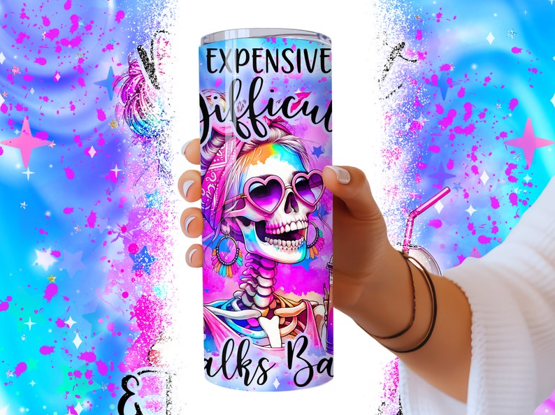 May include: A pink and purple stainless steel tumbler with a colorful skull design and the text "Expensive Tastes Difficult Walks Backwards".