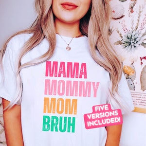 May include: White t-shirt with a distressed graphic design that reads "Mama Mommy Mom  Bruh" in pink, orange, and green. The text "Five Versions Included!" is in a pink circle.