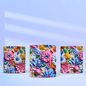 May include: Three white ceramic mugs with a colorful floral design. The flowers are 3D and appear to be made of paper or fabric. The mugs are arranged in a row on a light blue surface.