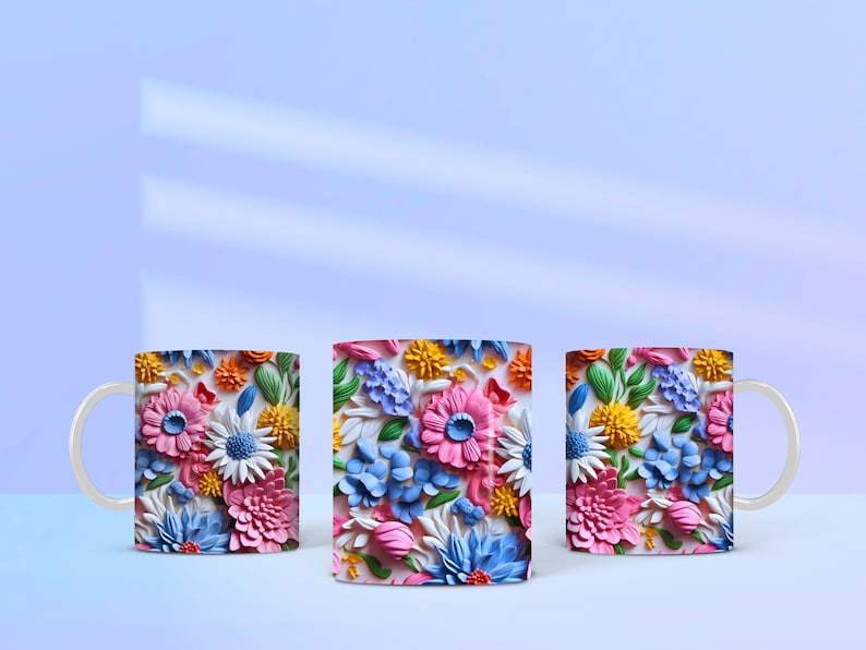 May include: Three white ceramic mugs with a colorful floral design. The flowers are 3D and appear to be made of paper or fabric. The mugs are arranged in a row on a light blue surface.