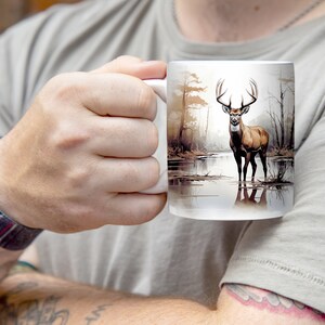 May include: White ceramic mug with a brown deer standing in a lake with trees in the background. The deer has large antlers.