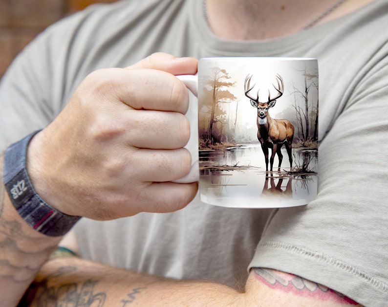 May include: White ceramic mug with a brown deer standing in a lake with trees in the background. The deer has large antlers.