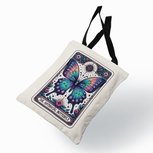 May include: A white tote bag with black straps features a colorful illustration of a butterfly with the text "The Antisocial Butterfly" printed on the front.