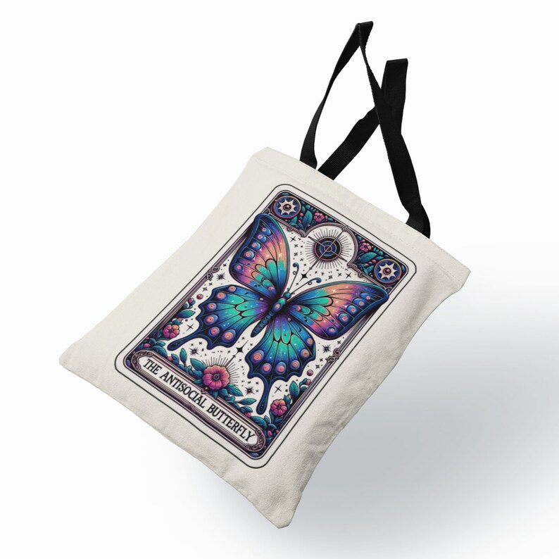 May include: A white tote bag with black straps features a colorful illustration of a butterfly with the text "The Antisocial Butterfly" printed on the front.