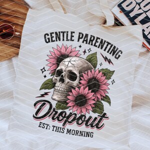 K&ouml;nnte beinhalten: Wei&szlig;e Einkaufstasche mit einem Totenkopf- und Blumenmotiv. Der Text lautet "Gentle Parenting Dropout Est: This Morning".