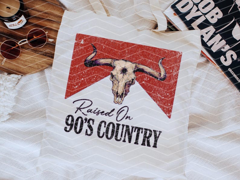 May include: White tote bag with a red and white graphic of a bull skull with the text "Raised On 90's Country".