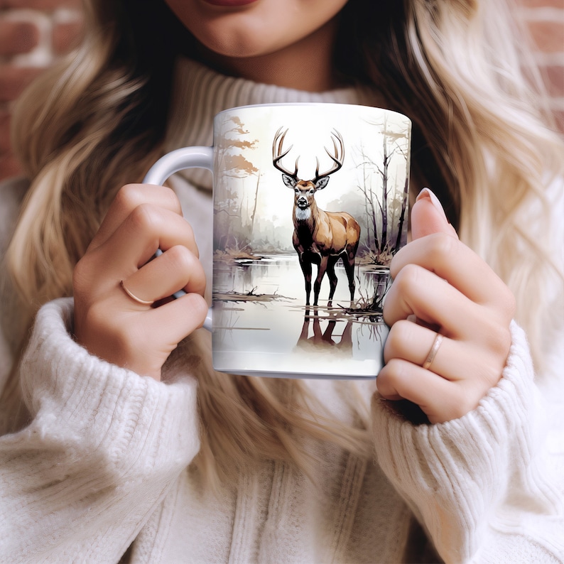 May include: White ceramic mug with a brown and white deer illustration. The deer is standing in a lake with trees in the background.
