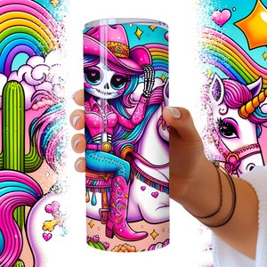 Puede incluir: Un vaso de acero inoxidable con un dise&ntilde;o colorido que presenta un esqueleto con un sombrero de vaquero montando un unicornio. El fondo es un cielo rosa y azul con un arco&iacute;ris y nubes.
