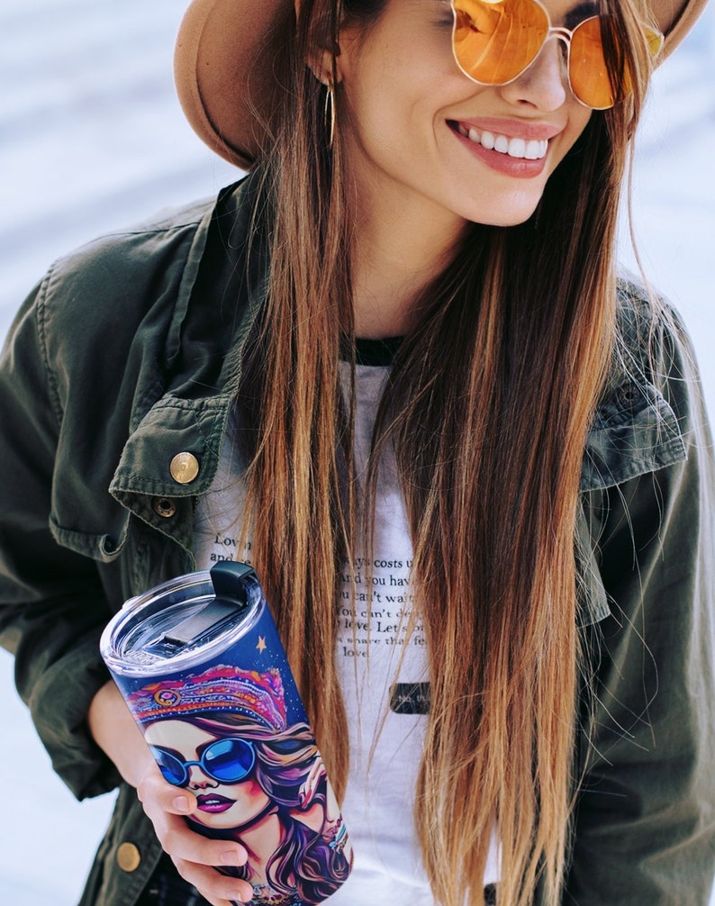 May include: A stainless steel tumbler with a colorful, psychedelic design featuring a woman wearing sunglasses and a headscarf. The tumbler has a lid with a straw.
