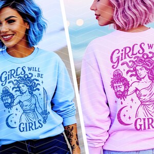 May include: Light blue sweatshirt with a graphic of Medusa holding a severed head and a sword, with the text "GIRLS WILL BE GIRLS". The design is in a darker shade of blue. The image shows the sweatshirt on a person.