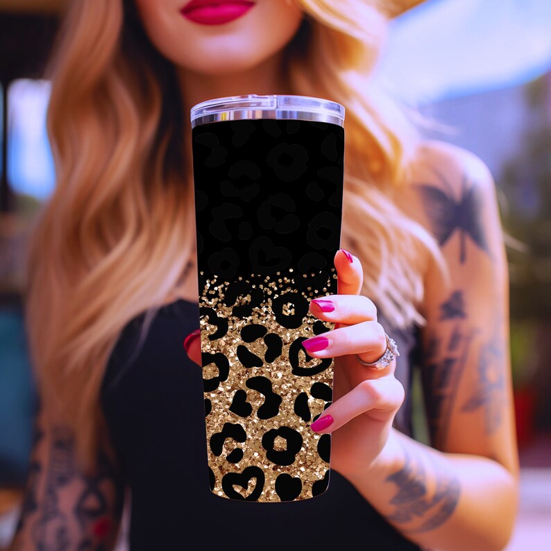 Op de afbeelding: Een zwarte en gouden roestvrijstalen beker met een luipaardprint. De beker heeft een gouden glitteraccent en is perfect voor het vasthouden van warme of koude dranken.