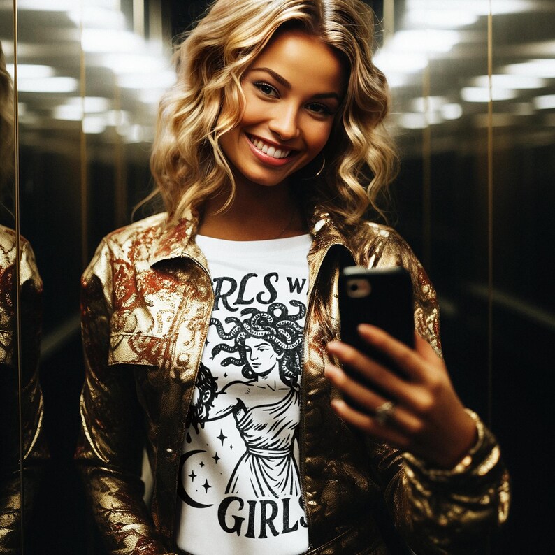 May include: A woman wearing a gold metallic jacket and a white t-shirt with a Medusa graphic and the text "RLS W GIRL" is taking a selfie with a smartphone. The background is a mirrored elevator.