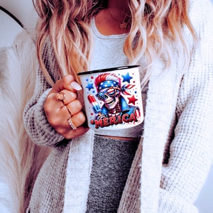 May include: White ceramic mug with a black rim and handle. The mug features a colorful graphic of a skeleton wearing a bandana and sunglasses, holding a popsicle. The text "MERICA" is printed on the mug.