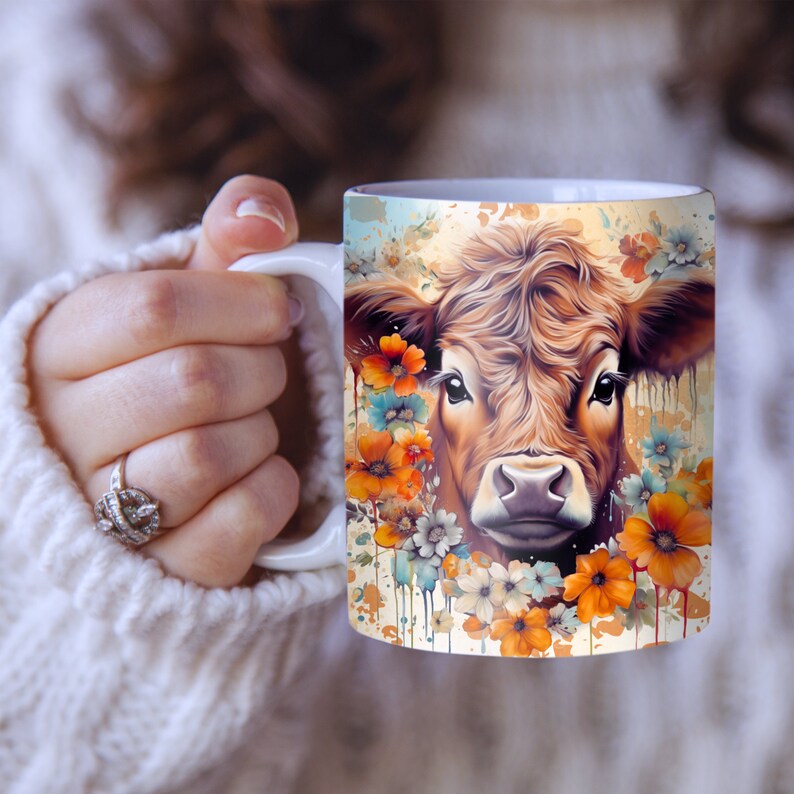 May include: White ceramic mug with a brown and white cow's face surrounded by orange, yellow, and blue flowers. The background is a light brown with white paint splatters.