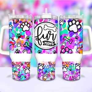 Puede incluir: Tres vasos de acero inoxidable con asa y tapa blancas. Los vasos están decorados con un diseño de acuarela colorido de huellas de patas y huesos. El vaso del medio tiene el texto "fur mama" en un círculo negro con un hueso blanco.