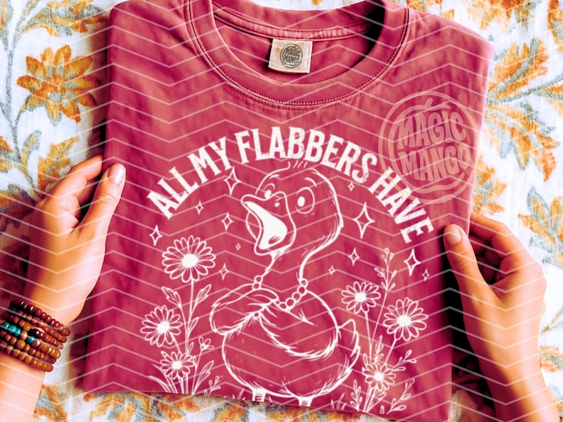 以下が含まれることがあります： ピンクのTシャツに、白いダックのグラフィックがプリントされています。ダックの周りに「All my flabbers have」というテキストが書かれています。グラフィックには、花と星も含まれています。