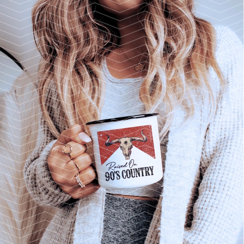 May include: White enamel mug with a black rim and handle. The mug has a red and white design with a skull and crossbones and the text "Raised On 90's Country".