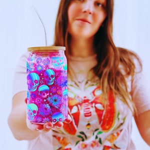 woman holding  a 16oz Libbey glass can with a wrap design sublimation PNG.  the design is neon colored skulls and flowers.  pretty colorful skull glass can wrap png for halloween