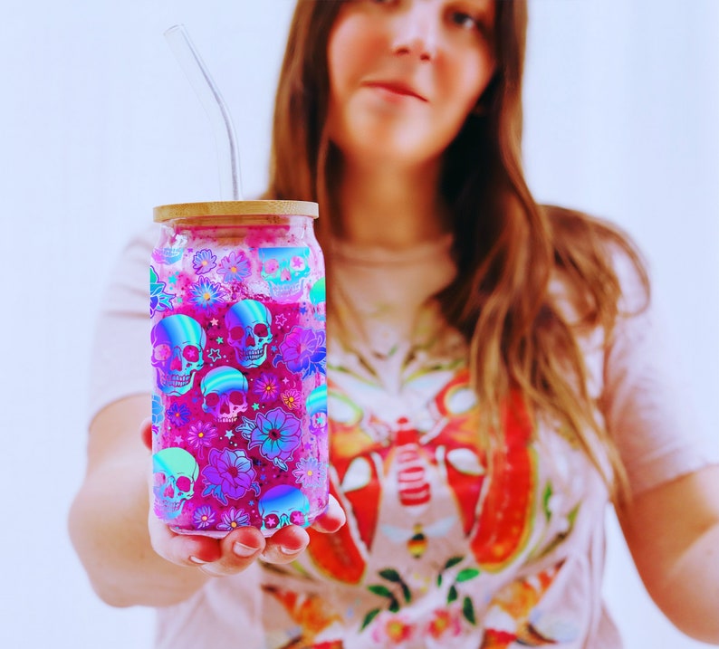 woman holding  a 16oz Libbey glass can with a wrap design sublimation PNG.  the design is neon colored skulls and flowers.  pretty colorful skull glass can wrap png for halloween