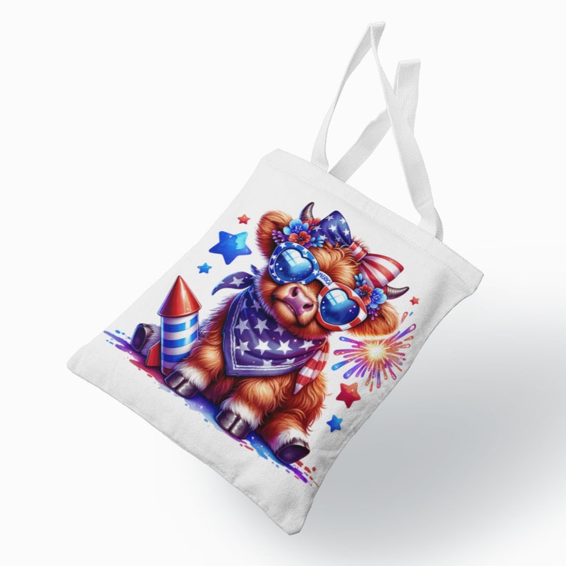 May include: A white tote bag with a cartoon Highland cow wearing red, white, and blue sunglasses and a bandana. The cow is holding a red, white, and blue firework. There are stars and fireworks in the background.