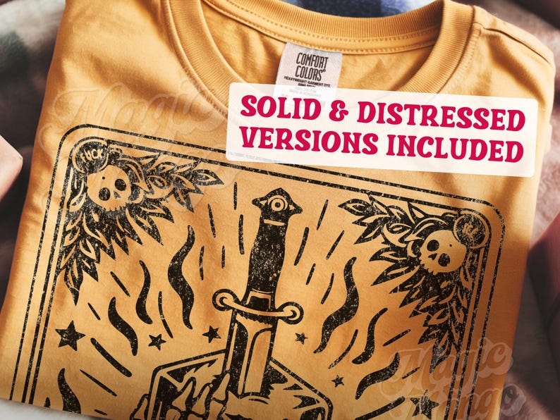 Pu&ograve; includere: T-shirt giallo senape con grafica nera invecchiata raffigurante un pugnale, teschi ed elementi floreali. La maglietta include il testo "SOLID & DISTRESSED VERSIONS INCLUDED" su un'etichetta bianca.