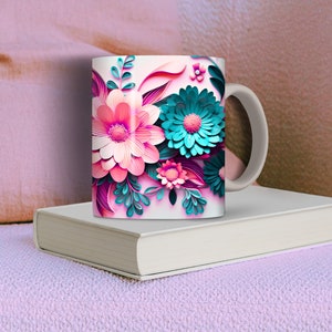 K&ouml;nnte beinhalten: Eine wei&szlig;e Keramiktasse mit einem farbenfrohen Blumendesign. Die Blumen sind rosa, blau und gr&uuml;n und haben eine papierartige Textur. Die Tasse hat einen wei&szlig;en Henkel.