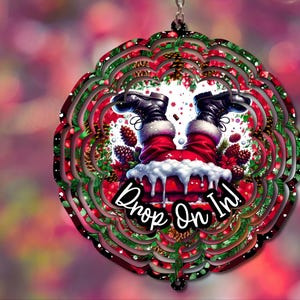 May include: A black metal wind spinner with a red and green Christmas design. Santa Claus is upside down with the text "Drop On In!" in a white circle.