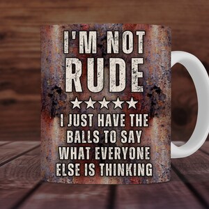 May include: A white ceramic mug with a rusty brown design. The mug features the text "I'M NOT RUDE" with five stars and the text "I JUST HAVE THE BALLS TO SAY WHAT EVERYONE ELSE IS THINKING".
