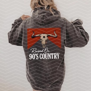 May include: A gray hoodie with a red and white graphic of a bull skull with the text "Raised On 90's Country" printed on the back.