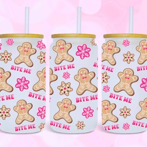 May include: Three white insulated tumblers with a wood lid and a straw. The tumblers have a pattern of gingerbread men and snowflakes with the text "Bite Me" repeated on each tumbler.