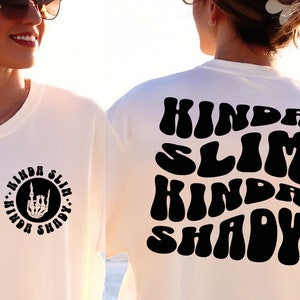 Puede incluir: Camiseta blanca con texto negro que dice "Kinda Slim Kinda Shady" en una fuente retro. El texto est&aacute; en la parte posterior de la camiseta. La parte delantera de la camiseta tiene un c&iacute;rculo negro con el mismo texto en una fuente m&aacute;s peque&ntilde;a y una mano de esqueleto haciendo el signo de rock and roll.