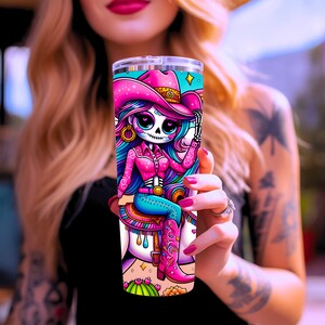 Puede incluir: Un vaso de acero inoxidable rosa y azul con una ilustraci&oacute;n colorida de un esqueleto con un sombrero de vaquero rosa montando un caballo blanco. El esqueleto tiene el pelo largo azul y lleva una camisa rosa y pantalones vaqueros azules.