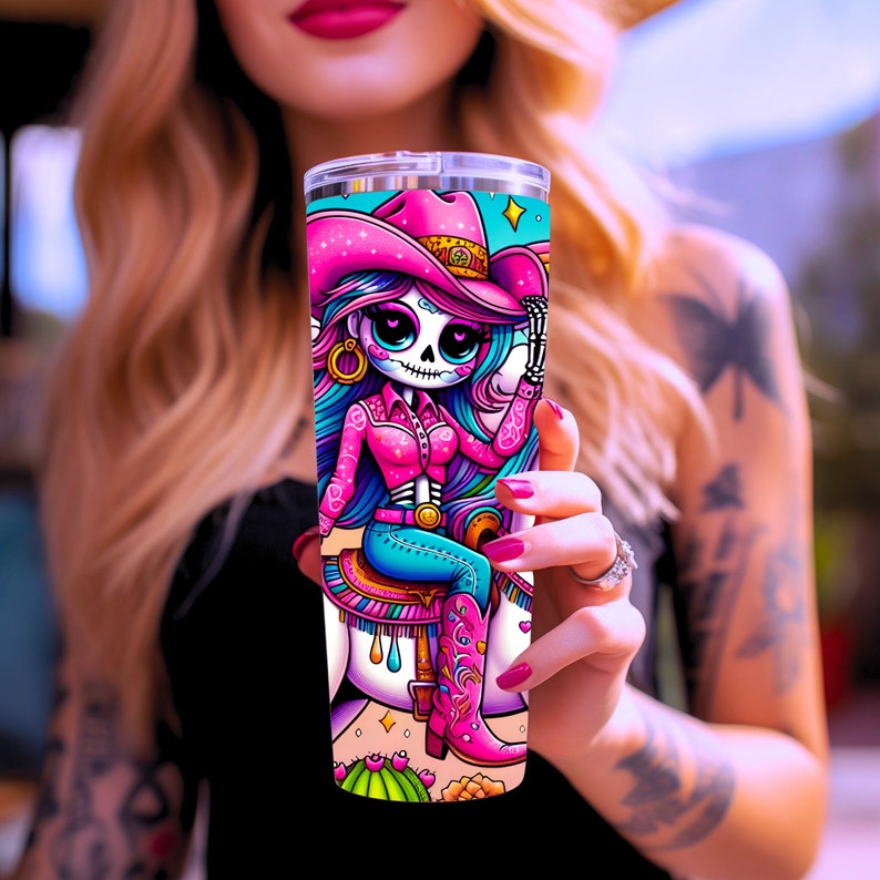 Puede incluir: Un vaso de acero inoxidable rosa y azul con una ilustraci&oacute;n colorida de un esqueleto con un sombrero de vaquero rosa montando un caballo blanco. El esqueleto tiene el pelo largo azul y lleva una camisa rosa y pantalones vaqueros azules.