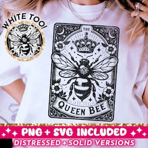 May include: A white t-shirt with a black and white graphic of a bee with a crown and the text "The Queen Bee". The graphic is in a vintage style with a gold border. The text "White Too!" is also on the shirt in a gold glitter font.