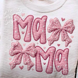 May include: Cream-colored sweatshirt with the word "MAMA" in pink, crocheted-style letters. Two pink bows and small hearts are also featured. The text "Magic Mama" is embroidered in the upper left corner.