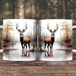 May include: Two white ceramic mugs with a deer standing in a lake in a forest scene. The deer is brown with large antlers. The mugs are 11 ounces.