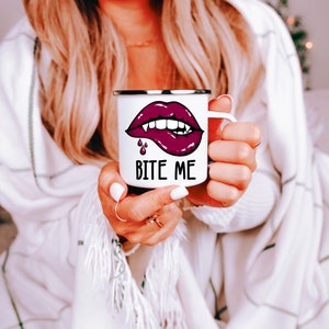 May include: White enamel mug with a red lip and fangs graphic and the text "Bite Me".