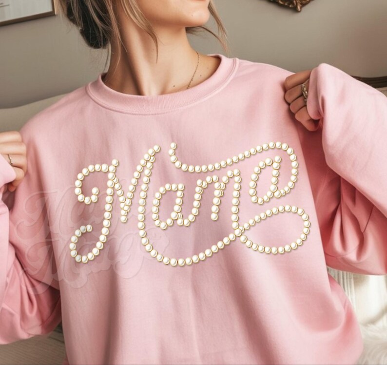 May include: A light pink sweatshirt with the word "Mama" spelled out in faux pearl beads. The sweatshirt has long sleeves and a crew neck. The design is centered on the chest.