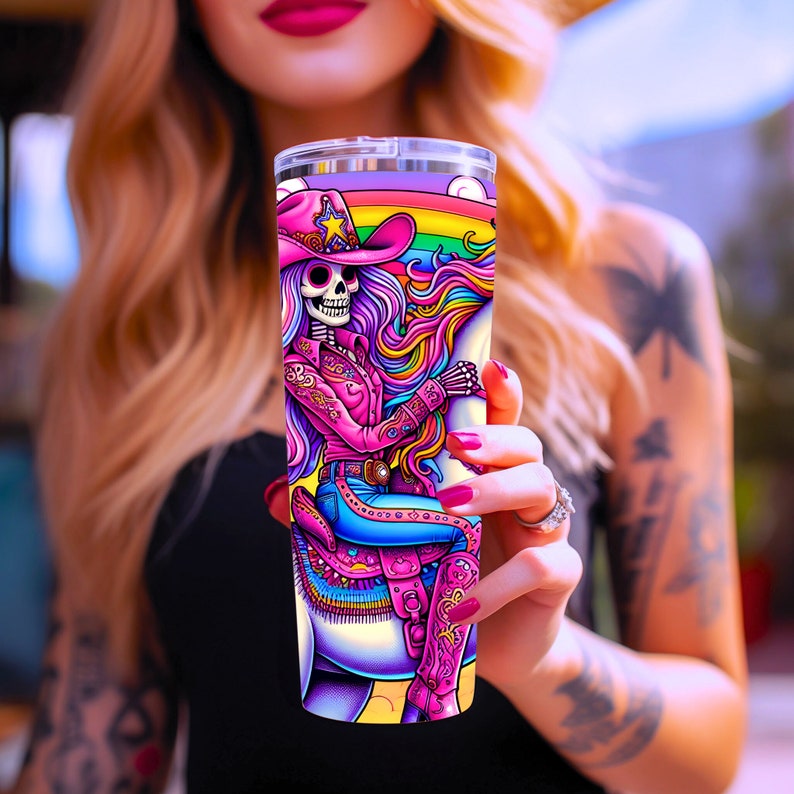 May include: A pink and purple stainless steel tumbler with a graphic of a skeleton wearing a pink cowboy hat and riding a unicorn with a rainbow mane.