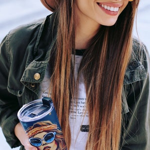 May include: A stainless steel tumbler with a black lid and a colorful graphic of a woman with sunglasses and a headband. The tumbler has a quote on it that reads "Love costs us nothing, but it gives us everything. Let's share this feeling of love."