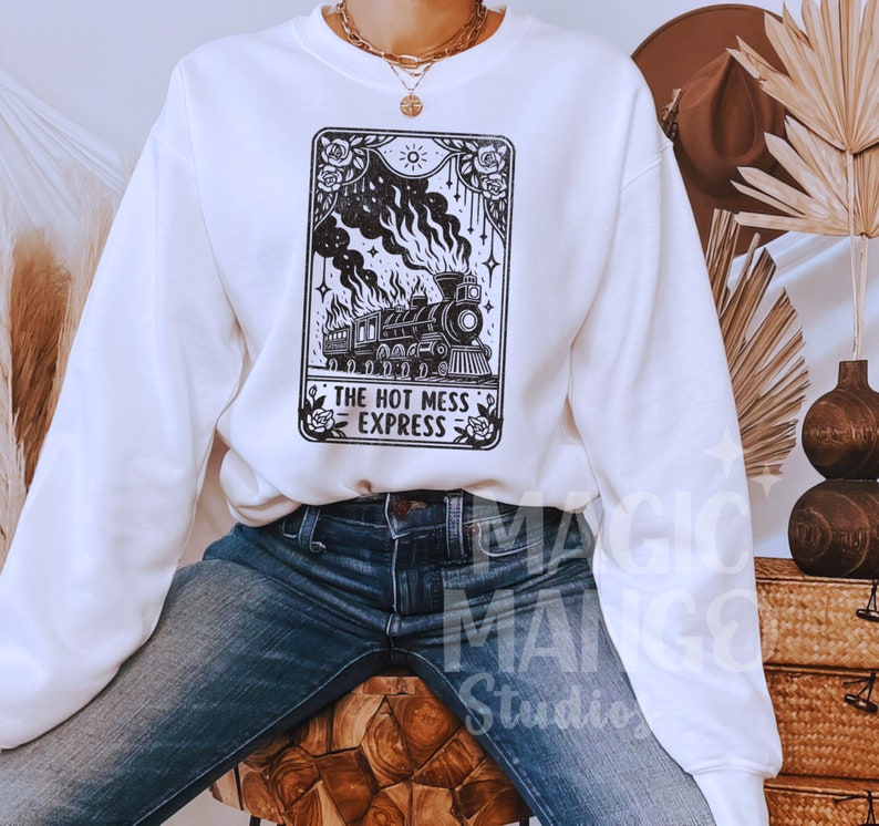May include: White sweatshirt featuring a black and white graphic of a vintage train with the text "THE HOT MESS EXPRESS". The design includes roses, a sun, and decorative elements. The sweatshirt is paired with blue jeans.