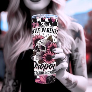 May include: A white tumbler with a pink and black design. The design features a skull with flowers and the text "Gentle Parenting Dropped Out This Morning".