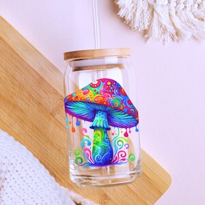 May include: A glass drinking jar with a bamboo lid and a straw. The jar has a colorful psychedelic mushroom design.