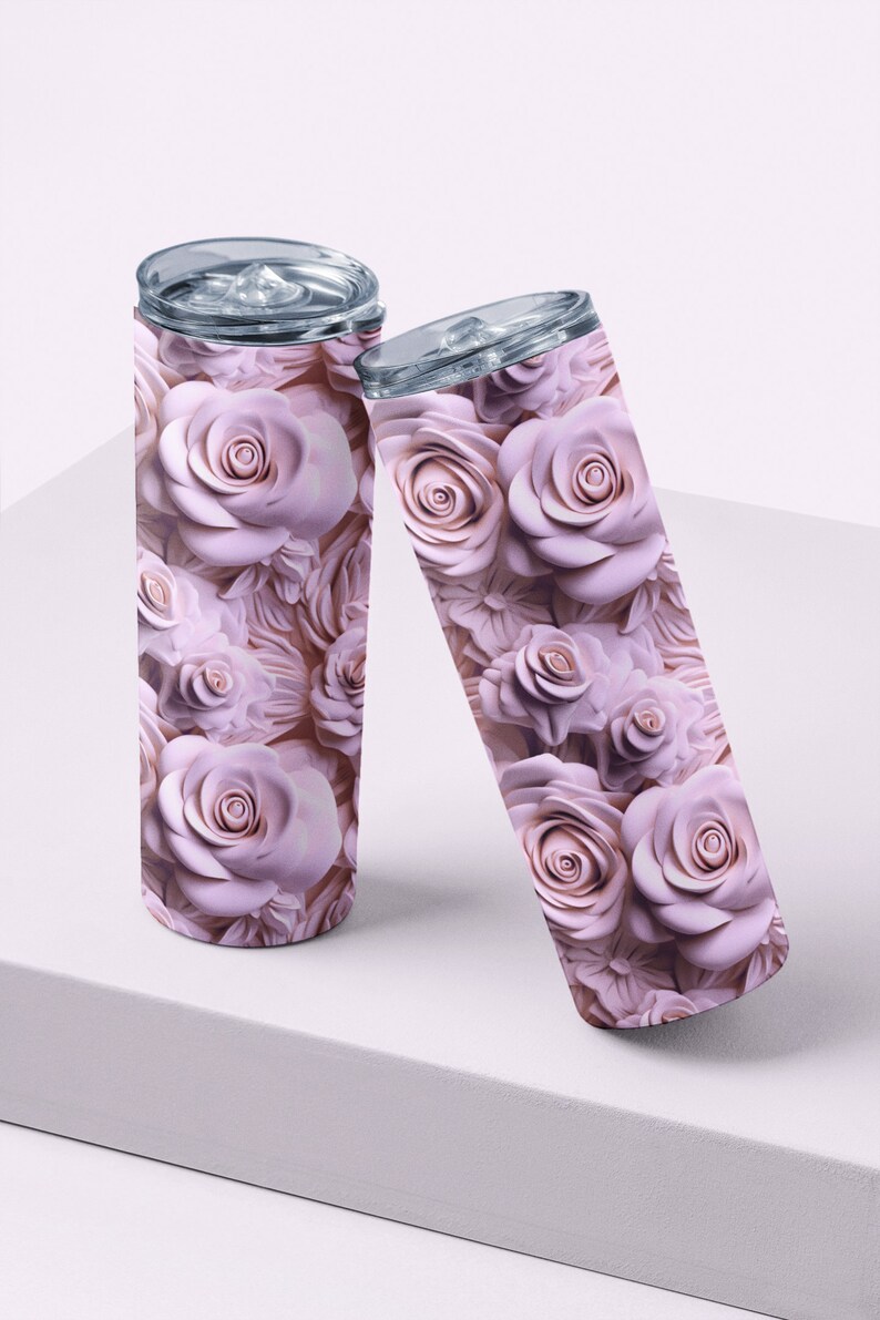 May include: Two stainless steel insulated tumblers with a floral rose pattern in shades of pink. The tumblers have clear lids and are displayed on a white surface. The rose design covers the entire surface of the tumblers.